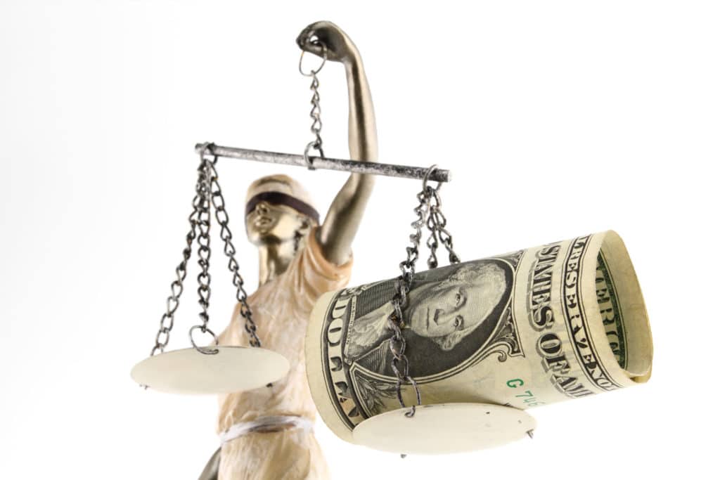 A blindfolded Lady Liberty holds the scales of justice, with one side heavily weighed by a roll of cash