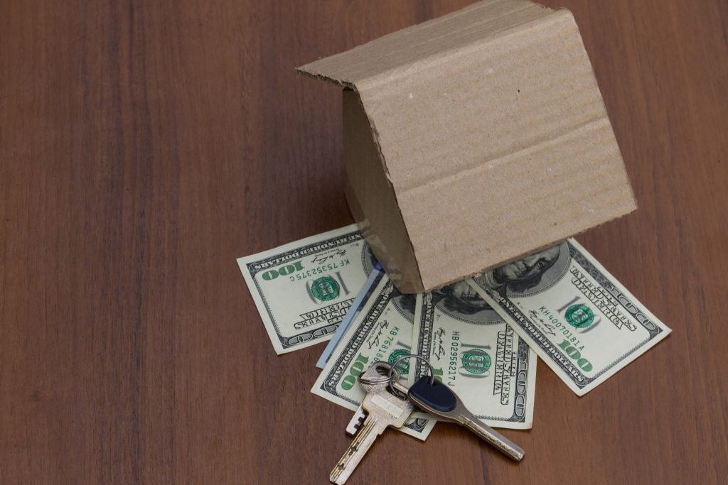 Small cardboard house, keys and dollars on wooden table